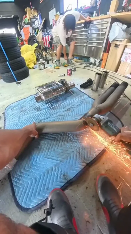マフラーの可変バルブを取り付ける作業を、作業者の目線で撮った動画のカット。グラインダーの火花が散っている