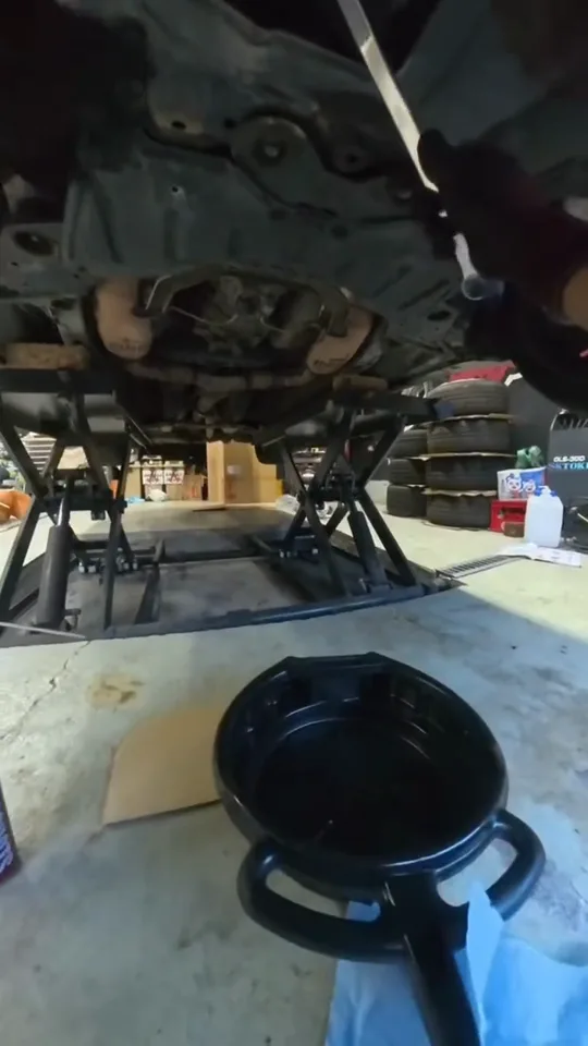 リフトで上げた車の下にオイル受けを置く、オイル交換の作業を作業者の目線で撮った動画のカット